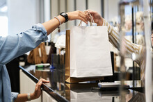 Unrecognizable Cashier Giving Paper Bags With Purchases To Unknown Customer At Clothing Store