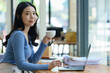 © Songsak C - Beautiful young asian business woman drinking coffee and using laptop computer while working in office.