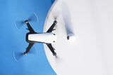Fototapeta  - Advanced White Quadcopter Drone Soaring Against a Blue Sky Background