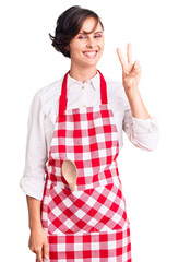 Wall Mural - Beautiful young woman with short hair wearing professional cook apron showing and pointing up with fingers number two while smiling confident and happy.