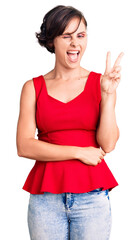 Poster - Beautiful young woman with short hair wearing casual style with sleeveless shirt smiling with happy face winking at the camera doing victory sign with fingers. number two.