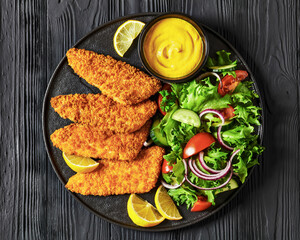 Poster - breaded fish fillet with salad on black plate