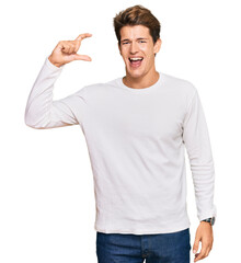 Wall Mural - Handsome caucasian man wearing casual white sweater smiling and confident gesturing with hand doing small size sign with fingers looking and the camera. measure concept.