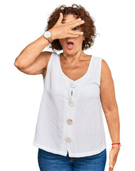 Sticker - Beautiful middle age mature woman wearing casual white shirt peeking in shock covering face and eyes with hand, looking through fingers with embarrassed expression.