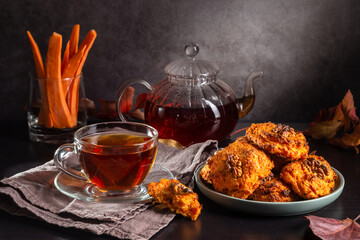 Wall Mural - Carrot cookies with walnuts and tea in a cup against a dark background