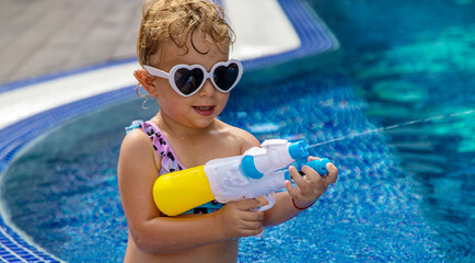 Poster - A child plays with a water pistol in the pool. Selective focus.