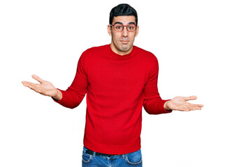 Wall Mural - Handsome hispanic man wearing casual clothes and glasses clueless and confused expression with arms and hands raised. doubt concept.