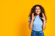 Woman with fingers crossed, hopeful look on yellow background