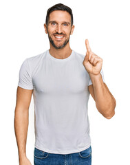 Sticker - Handsome man with beard wearing casual white t shirt showing and pointing up with finger number one while smiling confident and happy.