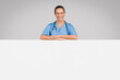 © Prostock-studio - Medical ad. Cheerful european female doctor leaning on big blank advertising board with free space for your text or offer