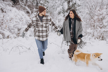 Wall Mural - Happy young couple with akita dog in forest on winter and snowly day