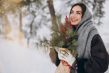 Wall Mural - Happy pretty smiling woman holding bouquet of pine tree in snowy forest in winter.