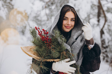 Wall Mural - Portrait of happy pretty woman holding winter pine bouquet and posing in snowy forest