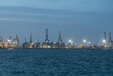 Fototapeta Miasto - Valencia, Valencia Spain - 05 05 2023: Cranes with beautiful lighting in the port on the blue sea in the evening