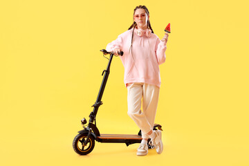 Wall Mural - Young woman with lollipop and electric scooter on yellow background