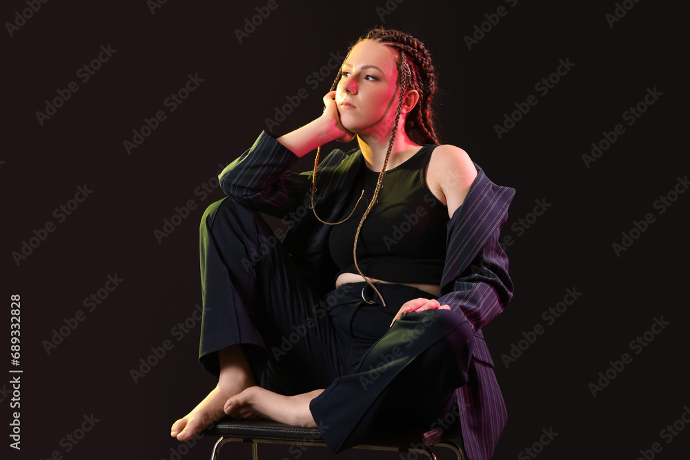 Young woman with dreadlocks sitting on dark background