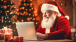 © mila103 - Santa Claus is using a laptop and smiling while sitting at the table at home.
