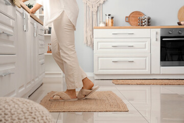 Poster - Woman on wicker carpet in light kitchen