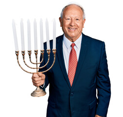 Sticker - Senior business man with grey hair holding menorah hanukkah jewish candle looking positive and happy standing and smiling with a confident smile showing teeth