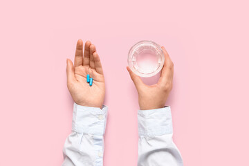 Wall Mural - Female hands with blue pills and glass of water on pink background