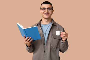 Poster - Handsome young man reading book and drinking coffee on beige background