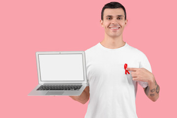 Wall Mural - Handsome young woman with red ribbon and laptop on pink background. World AIDS day concept