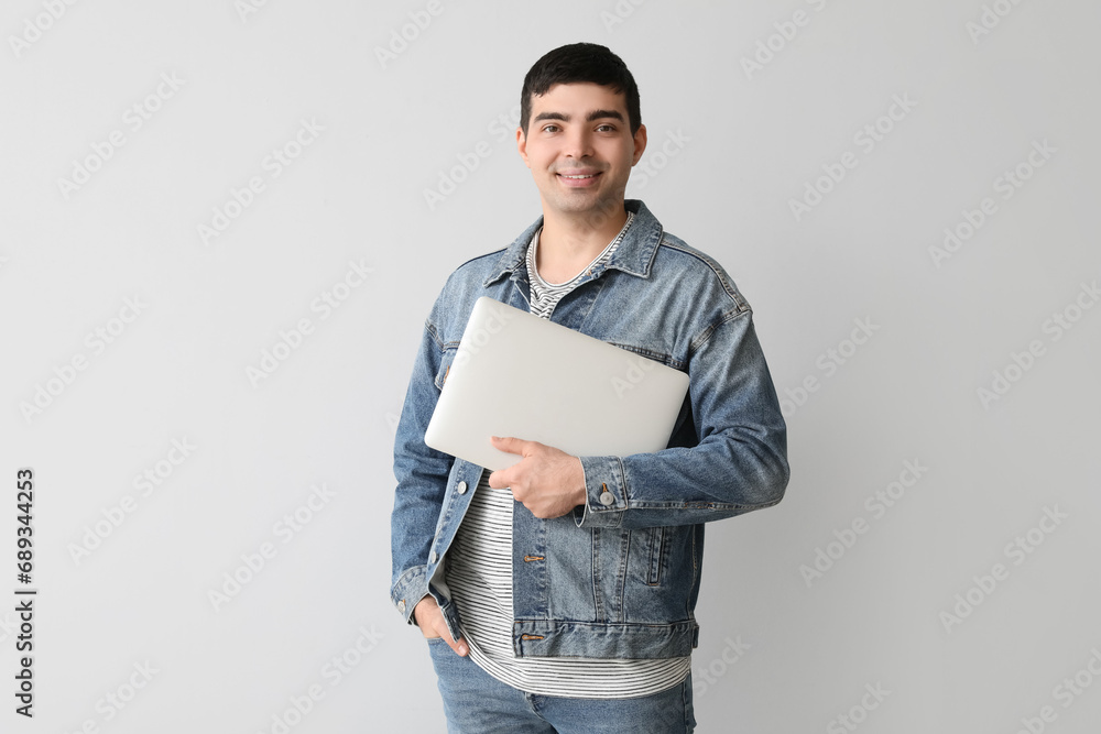 Happy young man with laptop on light background