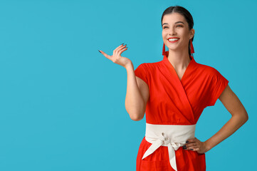 Poster - Beautiful young happy woman pointing at something on blue background. Chinese New Year celebration