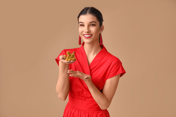 Poster - Beautiful young happy woman pointing at golden dragon figurine on brown background. Chinese New Year celebration