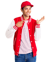 Poster - Young african amercian man wearing baseball uniform amazed and smiling to the camera while presenting with hand and pointing with finger.