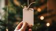 A hand holding a white gift tag, in the style of craftcore, blurry gift package in background wrapped in cardstock paper and hemp rope