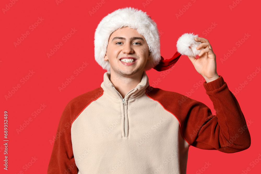 Happy young man in Santa hat on red background