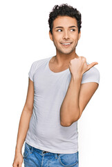 Wall Mural - Young handsome man wearing casual white t shirt smiling with happy face looking and pointing to the side with thumb up.