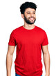 © Krakenimages.com - Young arab man with beard wearing casual red t shirt looking away to side with smile on face, natural expression. laughing confident.