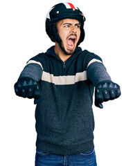 Wall Mural - Young hispanic man with beard wearing motorcycle helmet doing driving gesture angry and mad screaming frustrated and furious, shouting with anger. rage and aggressive concept.