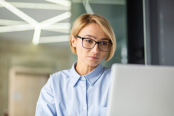 Portrait of a concentrated serious well-dressed office worker woman using a computer in a bright modern office.