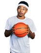 © Krakenimages.com - Young african american man holding basketball ball smiling looking to the side and staring away thinking.