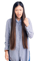 Wall Mural - Young beautiful chinese woman wearing casual shirt angry and mad raising fist frustrated and furious while shouting with anger. rage and aggressive concept.