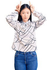 Poster - Young beautiful chinese woman wearing casual shirt doing funny gesture with finger over head as bull horns