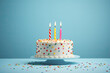 Tarta de cumpleaños de nata con virutas de chocolate de colores con tres velas encendidas, sobre plato y fondo azul claro. concepto cumpleaños y aniversarios