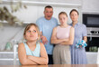 Portrait of frustrated tween girl in home kitchen, frowning with arms crossed. Disgruntled parents reprimanding her while standing with eldest daughter on blurred background. Emotional abuse concept