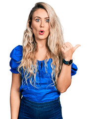 Wall Mural - Young blonde woman wearing casual clothes surprised pointing with hand finger to the side, open mouth amazed expression.