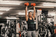 © Dusan Petkovic - A strong sportswoman is lifting dumbbells in the air and working out in a gym.