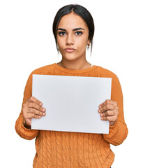 Young brunette woman holding blank empty banner thinking attitude and sober expression looking self confident