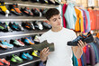 © JackF - Guy view specialized shoes in store, near showcase with summer trecking cross shoes, buyer think about advantages and disadvantages of hiking shoes