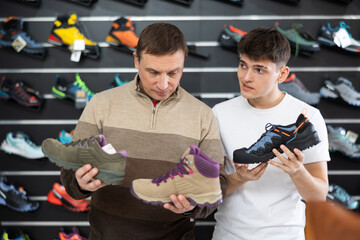 Wall Mural - Man with his son young guy chooses specialized shoes in store, near showcase with autumn trekking cross shoes, buyers talk about advantages and disadvantages of hiking boots