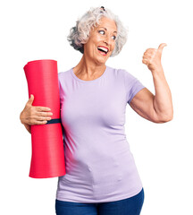 Wall Mural - Senior grey-haired woman holding yoga mat pointing thumb up to the side smiling happy with open mouth