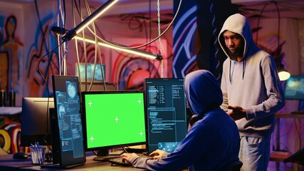 Wall Mural - Hacker using green screen PC to do data breaches and financial theft in graffiti painted hideout. Rogue programmers using chroma key monitor for stealing users bank account credentials