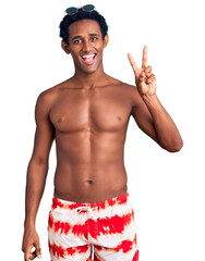 Canvas Print - African handsome man wearing swimsuit and sunglasses showing and pointing up with fingers number two while smiling confident and happy.