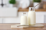 Glass bottles of fresh milk with straws on wooden table